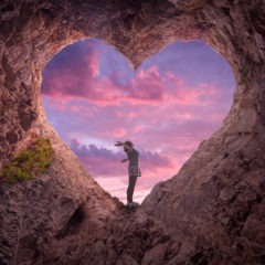 Young woman in heart shape cave towards the beautiful sky